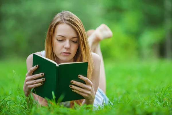 Молодая женщина лежит на траве и читает книгу Стоковая Картинка