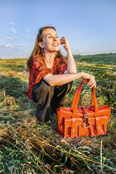 Kvinna med röd väska sitter i fältet — Stockfoto