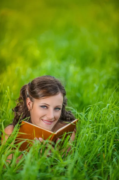 Νεαρή γυναίκα ξαπλωμένη στο γρασίδι και το βιβλίο ανάγνωσης — Φωτογραφία Αρχείου