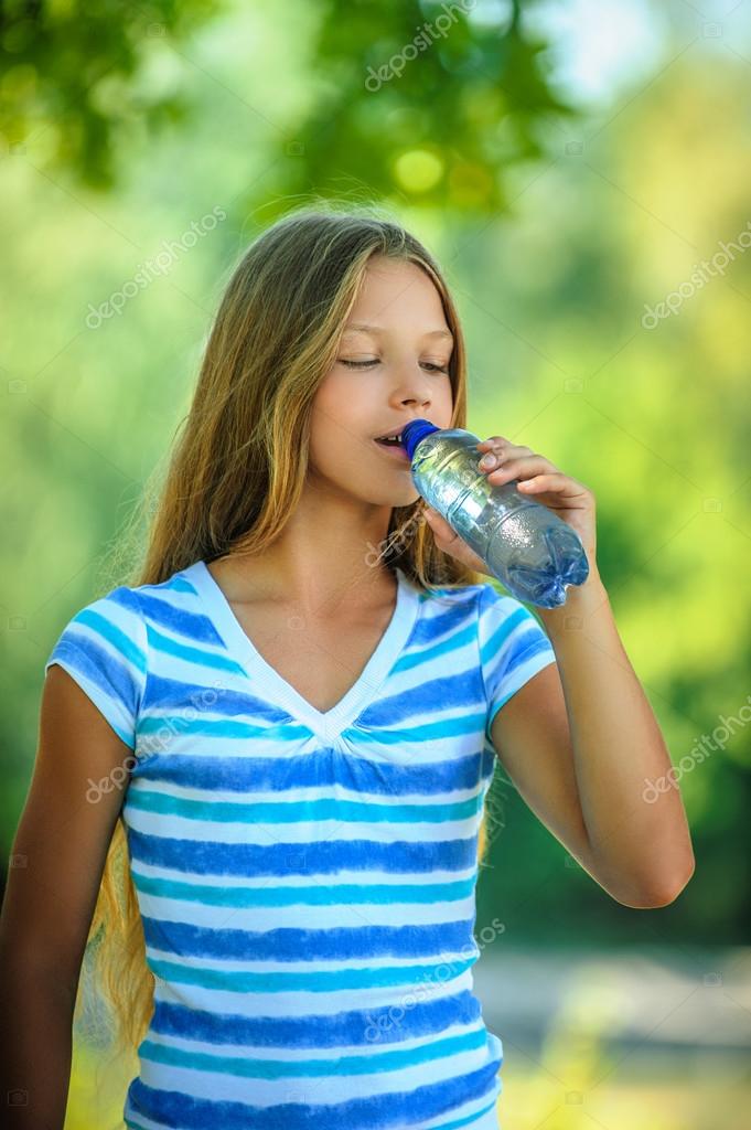 Teenage girl drinks water from bottle Stock Photo by