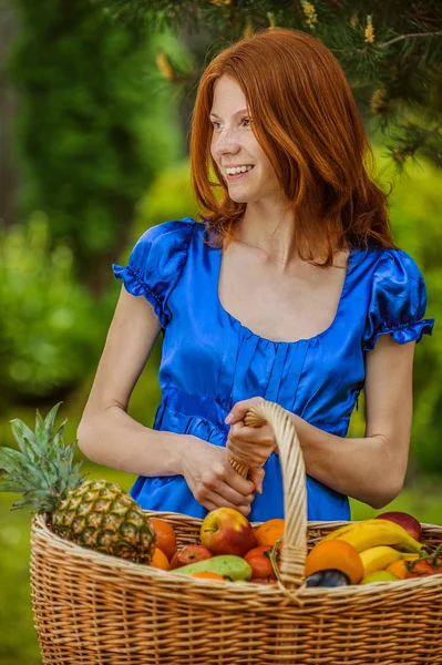 Κοκκινομάλλης χαμογελώντας νεαρή γυναίκα με ένα καλάθι με φρούτα — Φωτογραφία Αρχείου