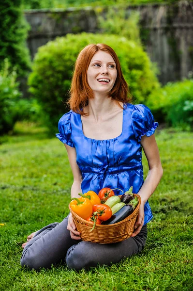 Jonge vrouw in zittend op het gazon met plantaardige mandje — Stockfoto