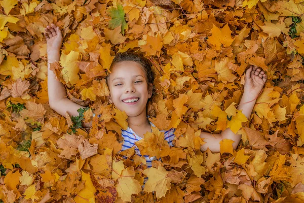Little girl buried in autumn leaves yellow — Stock Photo, Image