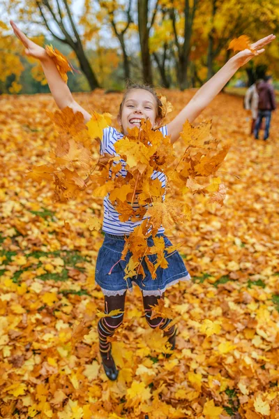 Menina saltando no fundo de folhas amarelas — Fotografia de Stock