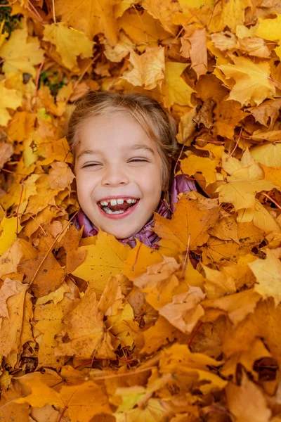 Liten flicka begravd i höst lämnar gul — Stockfoto