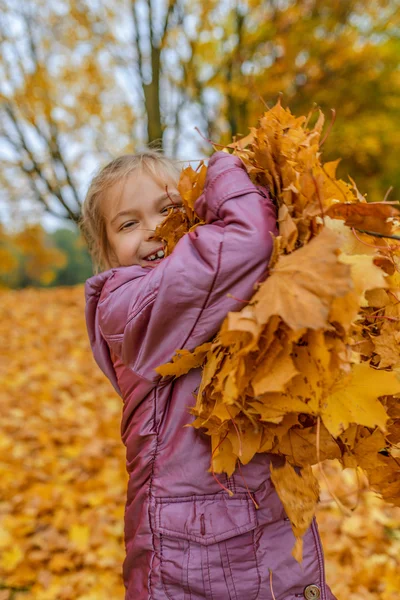 Küçük kız sarı yapraklar arka plan üzerinde atlama — Stok fotoğraf