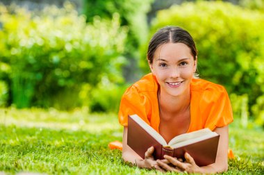 genç kadın kitap ile çim üzerinde yalan