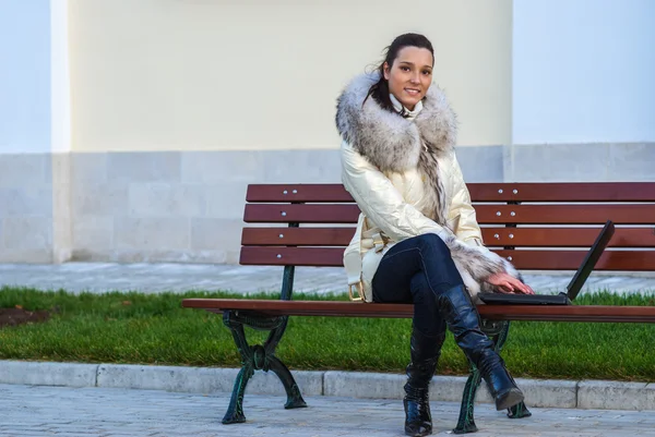 Жінка в білому пальто сидить на лавці — стокове фото