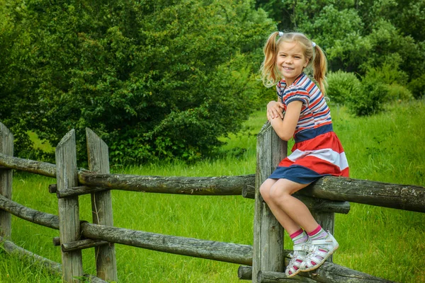 Little smiling girl sitting on wooden fence — Stock Photo, Image