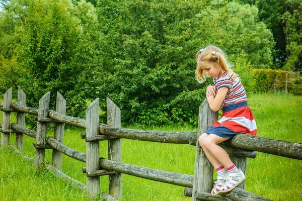 Little sad girl sitting on wooden fence — Stock Photo, Image