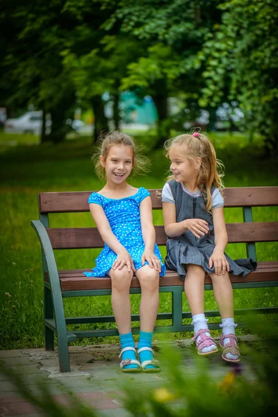两个面带笑容的小姐妹坐在长凳上 — 图库照片