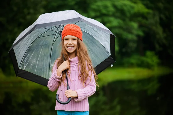 Kleines schönes Mädchen im rosafarbenen Pullover mit Regenschirm — Stockfoto