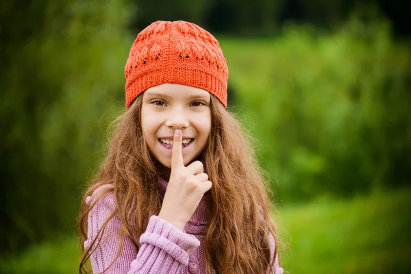 Pequeña chica sonriente pone el dedo en su boca — Foto de Stock