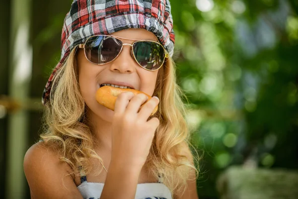 격자 무늬 모자 베이글을 먹는 어린 소녀 — 스톡 사진