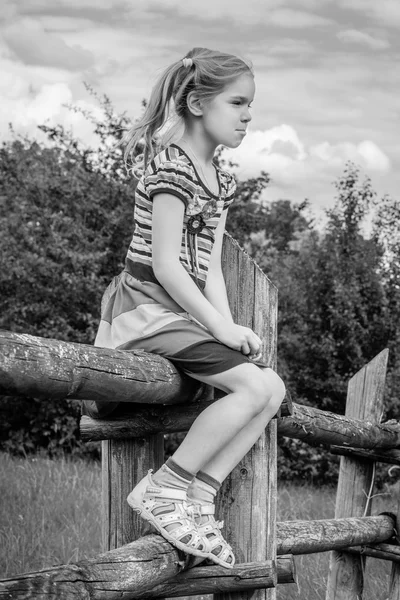 Маленькая грустная девочка сидит на деревянном заборе — стоковое фото