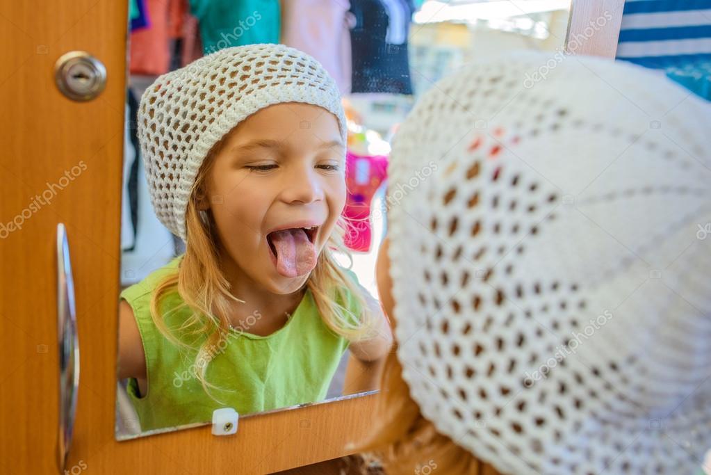 Little girl looks in mirror and shows tongue — Stock Photo