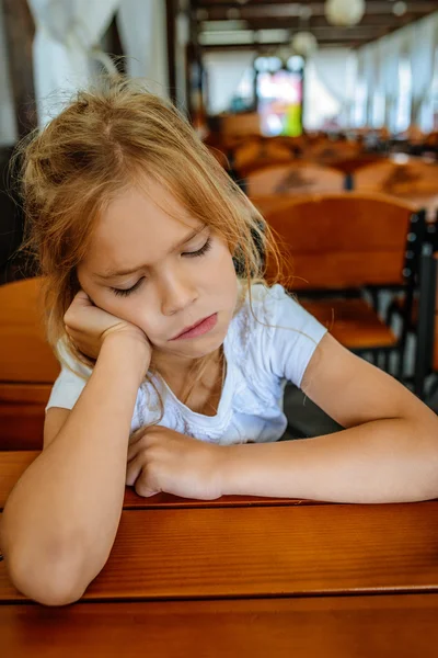 Menina triste sentada em uma mesa de madeira — Fotografia de Stock