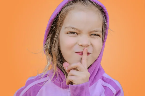 Little smiling girl in puts forefinger to lips — Stock Photo, Image