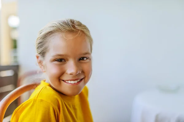 Liten flicka i gul blus sitter på en stol — Stockfoto