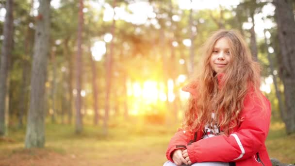 Улыбающаяся маленькая девочка в красной куртке в осеннем парке — стоковое видео