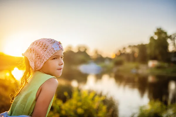 Kleine mooie peinzende meisje in de buurt van lake bij zonsondergang — Stockfoto