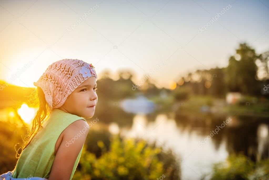Little beautiful pensive girl near lake at sunset