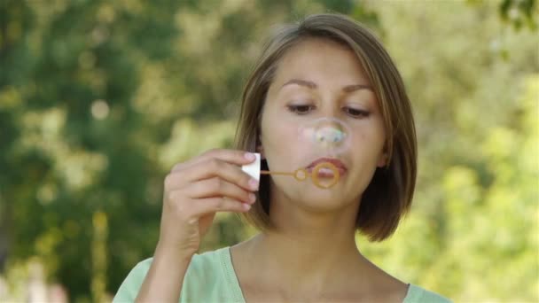 Young beautiful woman blows soap bubbles in park — Stock Video