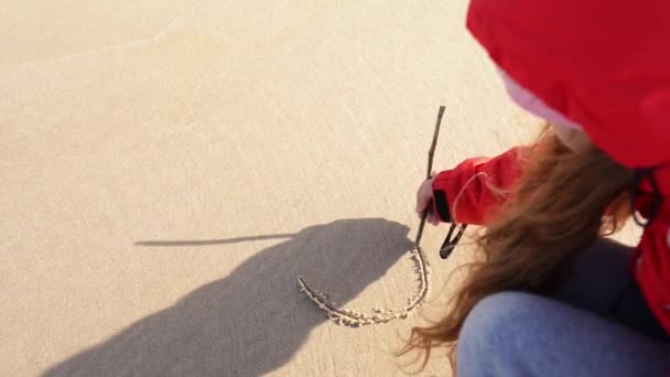 Girl draws on sand a little sun with rays — Wideo stockowe