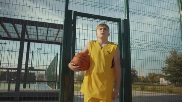 一个带着球在篮球场上行走的小男孩 — 图库视频影像
