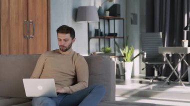 Young man working on a laptop on the couch.