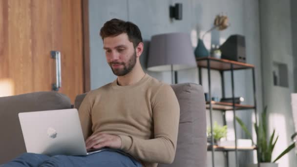 Νεαρός ευτυχισμένος άνθρωπος πληκτρολογώντας σε φορητό υπολογιστή από το σπίτι — Αρχείο Βίντεο