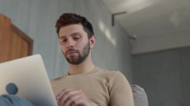 Young guy working on a laptop on the couch. Man typing with laptop on couch