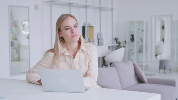 Tänkte flicka vid skrivbordet med en laptop i ett vitt rum. Porträtt av attraktiv kvinna hemma — Stockvideo