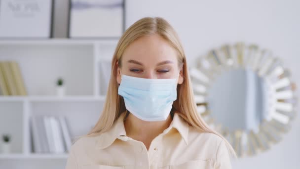 Mujer joven quitándose su máscara médica azul. Joven chica sonriente quitándose la máscara en el interior — Vídeos de Stock