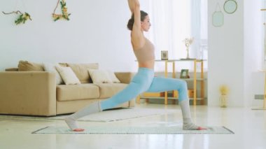 Spor giyimli genç bir kız evde antrenman yapıyor. Odada yoga yapan çekici bir kadın.