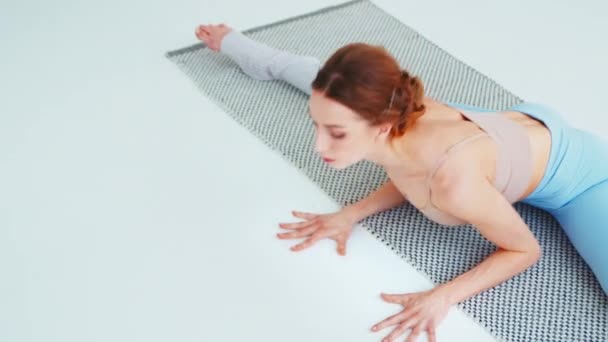 Attraktive Frau turnt auf einer Yogamatte auf weißem Boden. Junge Frau macht Pilates — Stockvideo