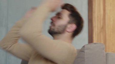 Genç adam ellerini başının üstüne atmış kanepede dinleniyor. Genç erkek, sakin bir atmosferde kanepede dinleniyor.