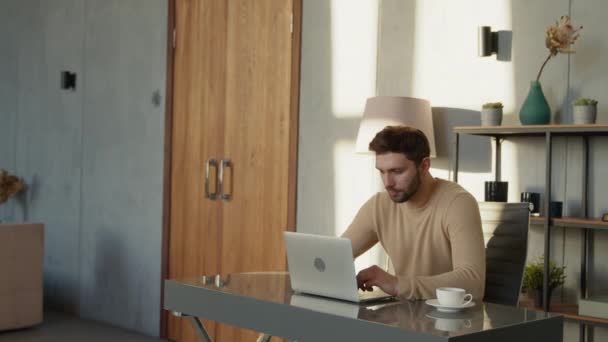 Un uomo serio che digita in cerca di idee alla scrivania di casa. Uomo emotivo con laptop al lavoro — Video Stock