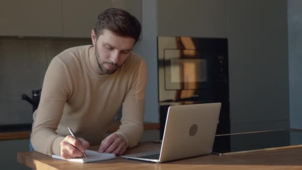 Grave giovane uomo che comunica in diretta video usando computer, microfono e webcam mentre è in cucina — Video Stock