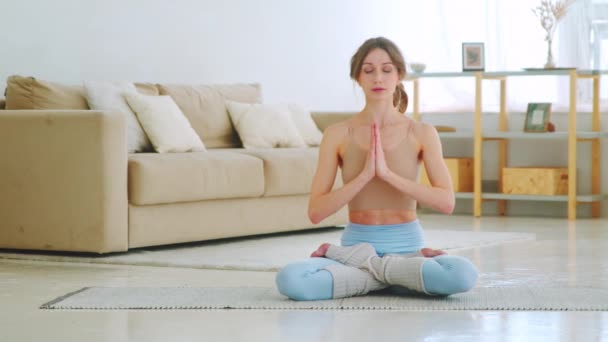 Aantrekkelijk sportief meisje zittend in lotuspositie met handen in de namaste. jong meisje doet yoga met gesloten ogen — Stockvideo