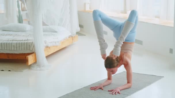 Attraktives Mädchen beim Handstand drinnen. Junges Mädchen macht Yoga auf der Matte — Stockvideo