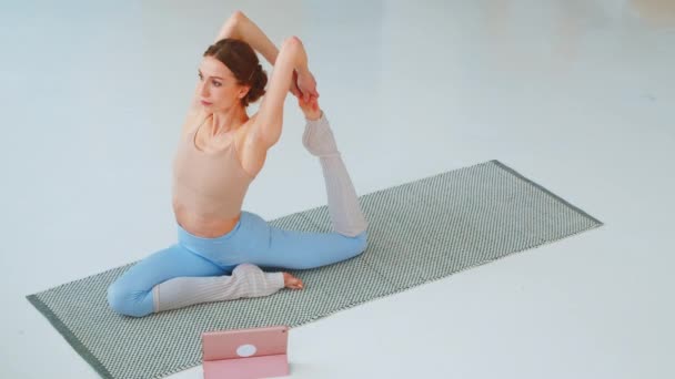 Jeune femme est engagée dans la formation en ligne. Femme athlétique faisant du yoga sur un plancher — Video