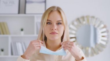 Genç ve çekici bir kız mavi bir maske takıyor. Tıbbi maskeli güzel bir kadın kameraya bakıyor.
