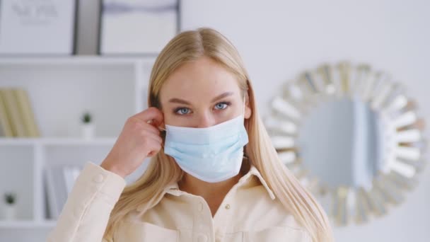 Menina atraente jovem tirando a máscara azul médica. Mulher sorridente bonita sem máscara médica olhando para a câmera — Vídeo de Stock