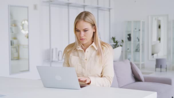 Leende tjej som skriver på en laptop i ett vitt rum. Ung kvinna chattar med vänner sittande i vitt rum — Stockvideo