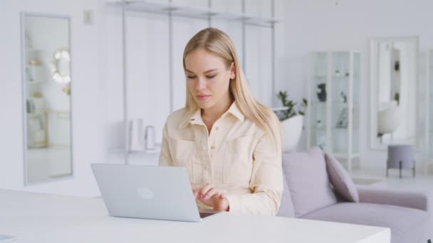 Úspěšná žena píšící na notebook v bílé místnosti. Mladá žena dostává dobré zprávy, zatímco sedí v bílém pokoji — Stock video