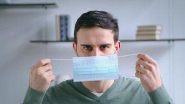 Genç bir adam mavi bir tıbbi maske takıyor. Genç adam maske takıyor.