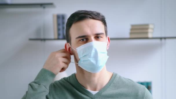 Giovane maschio attraente togliersi una maschera medica blu. Giovane uomo sorridente quando toglie la maschera — Video Stock
