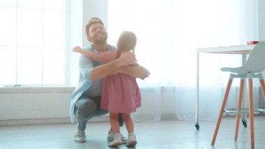 Genç baba, iç mekanda küçük kızına sarılıyor. Babalar Günü