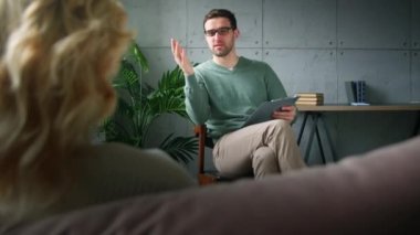 Genç, profesyonel bir psikoterapist bir hastaya depresyonun nedenlerini açıklıyor. Psikoterapide panosu olan genç bir adam.